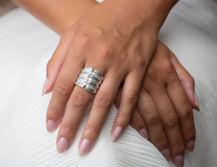 Close-up of hands with large scallop silver silver ring on a white fabric background