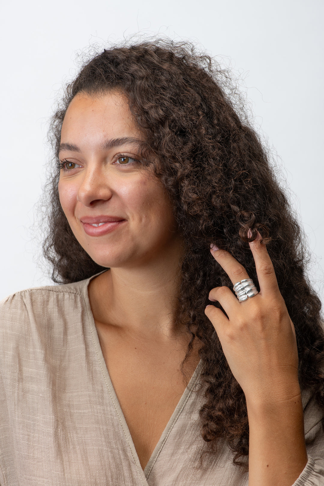 Woman with curly hair wearing a beige top and large scallop silver ring on a plain background