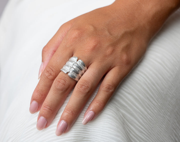 Hand wearing large scallop silver silver ring on a white background