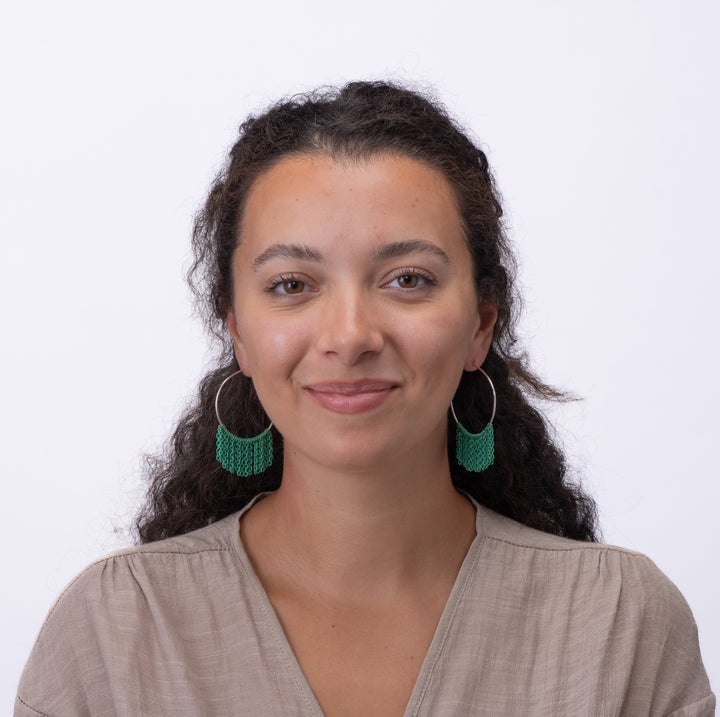Woman wearing silver Lieah hoop earrings with green fringe against a white background