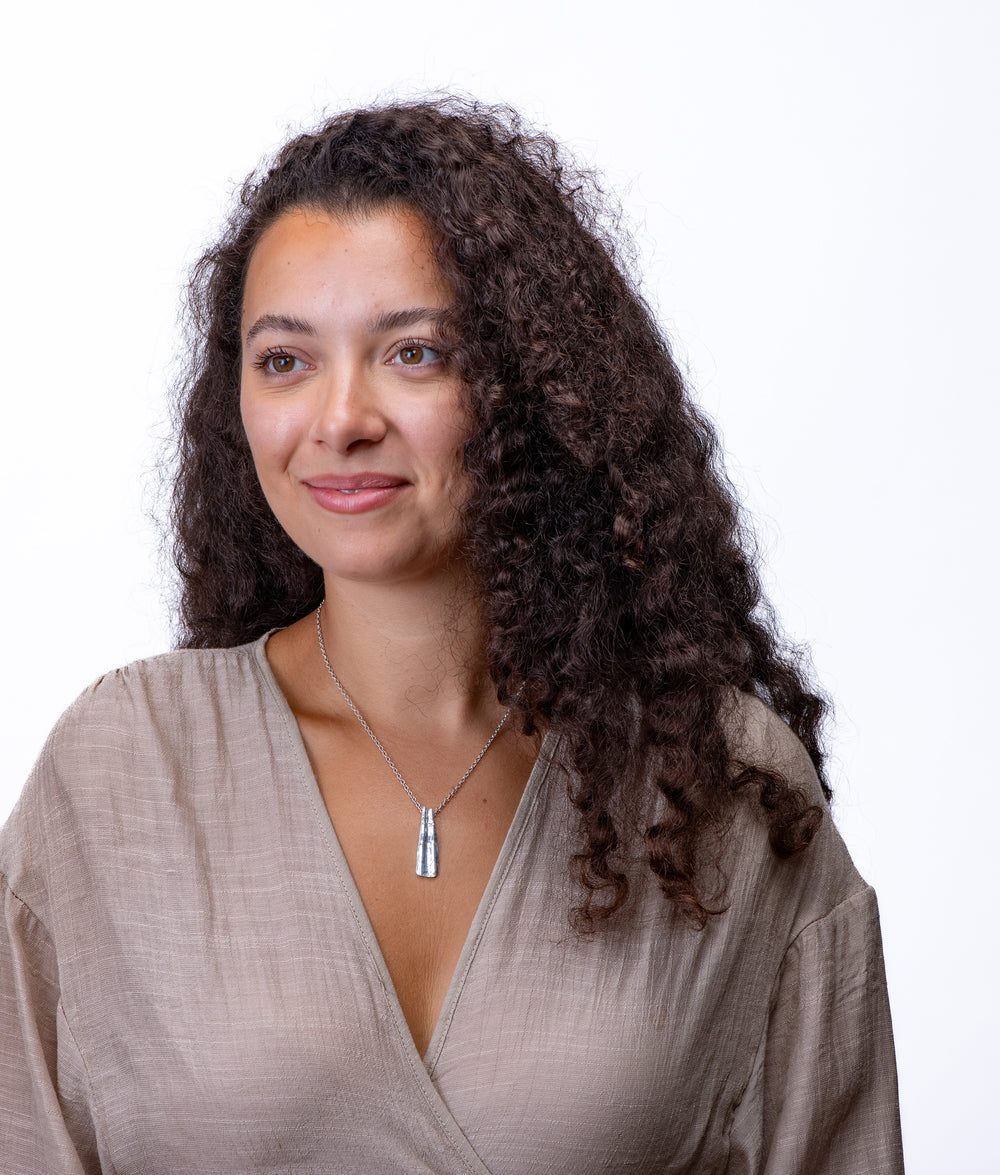 Woman with long, wavy hair wearing a silver scallop bar pendant necklace on a white background