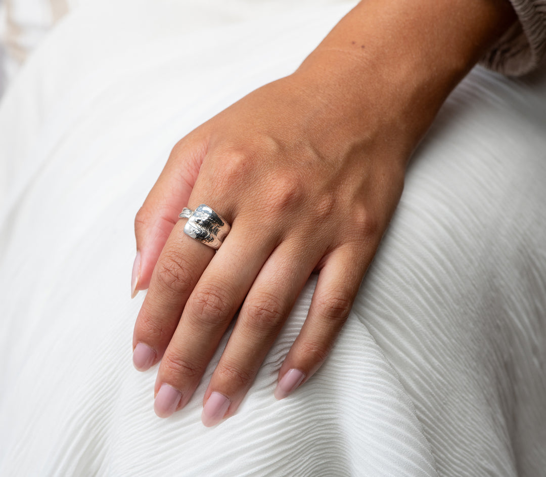 Hand wearing a silver wrap ring on a white fabric background