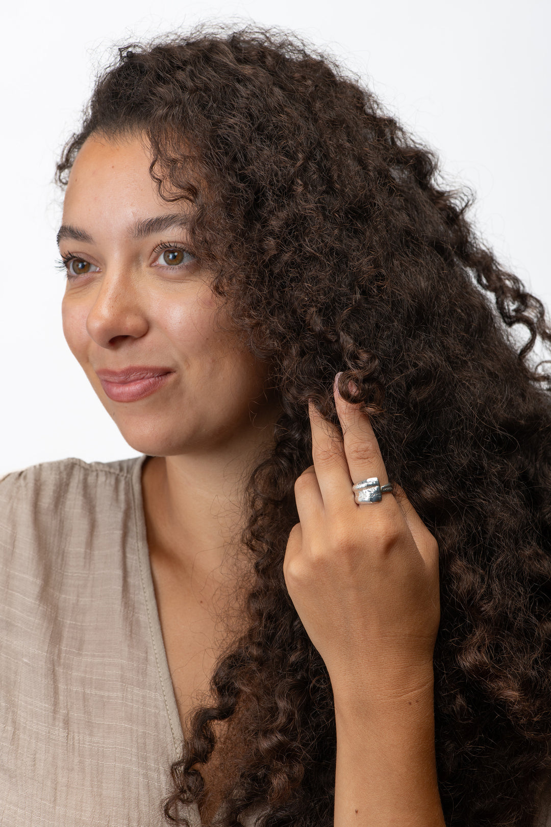Woman with curly hair touching her ear against a white background wearing a small scallop silver wrap ring. 