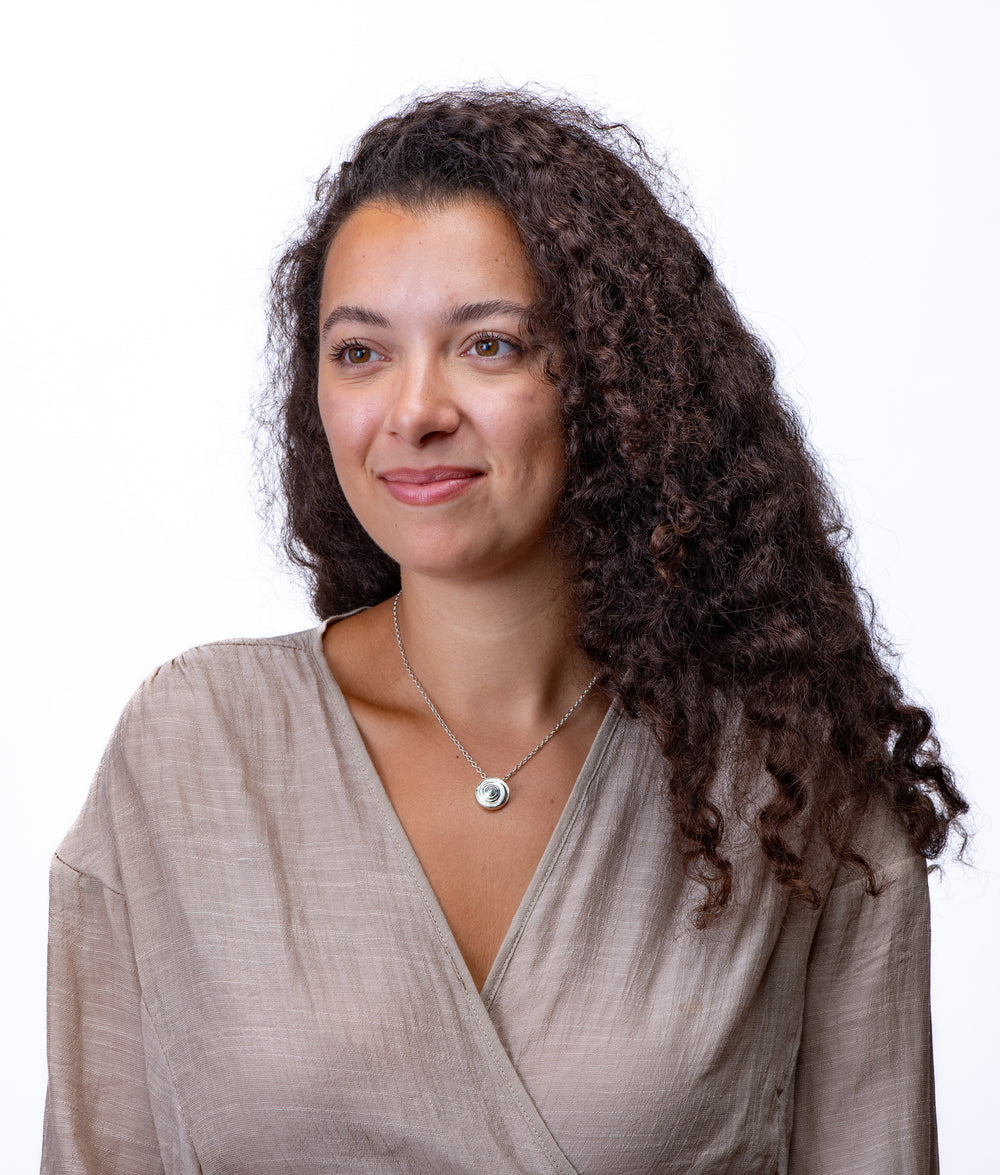 Woman with curly hair wearing a beige top and swirl shell necklace on a white background