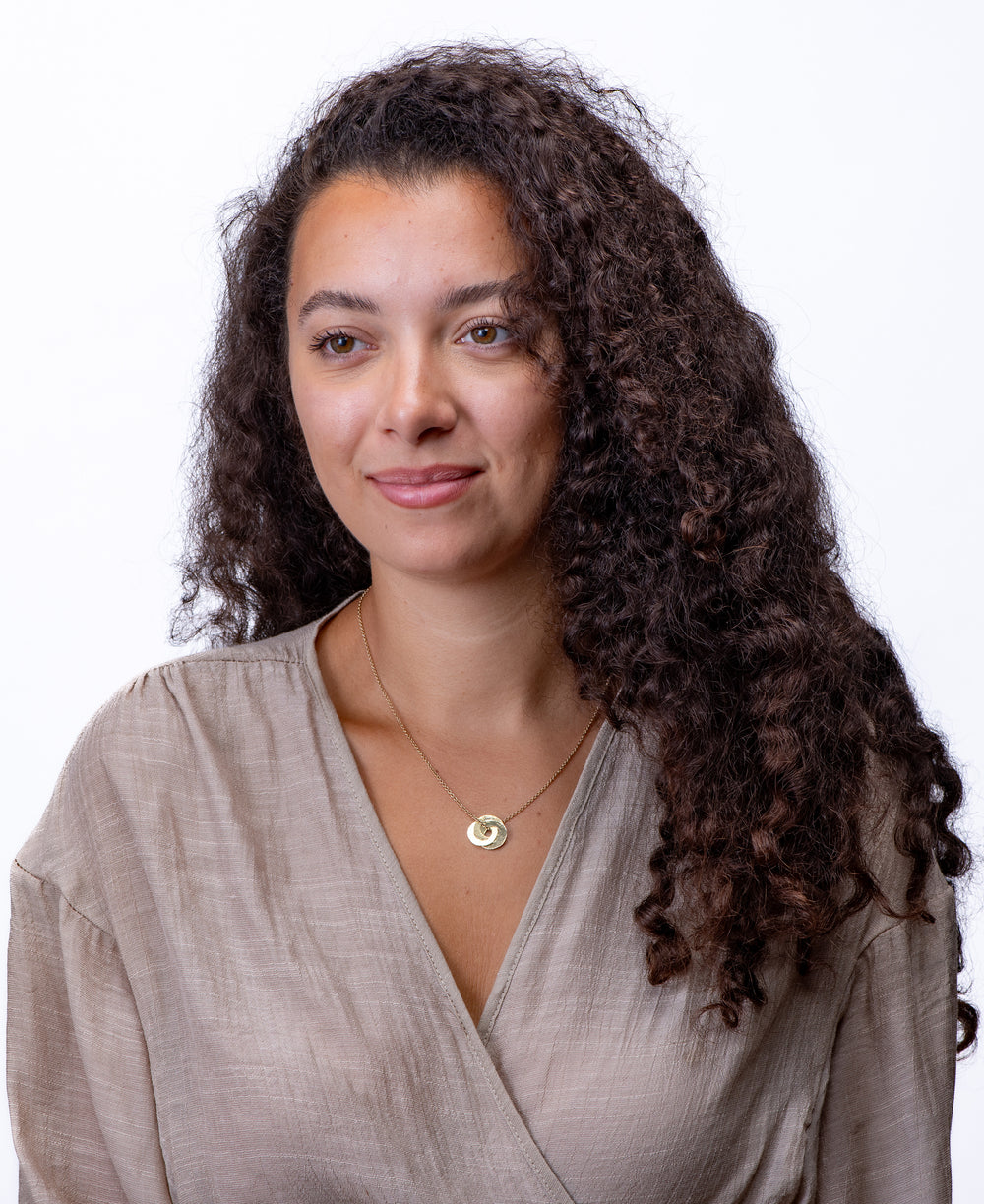 Woman with long, curly hair wearing a two tone gold and silver necklace with beige top on a white background