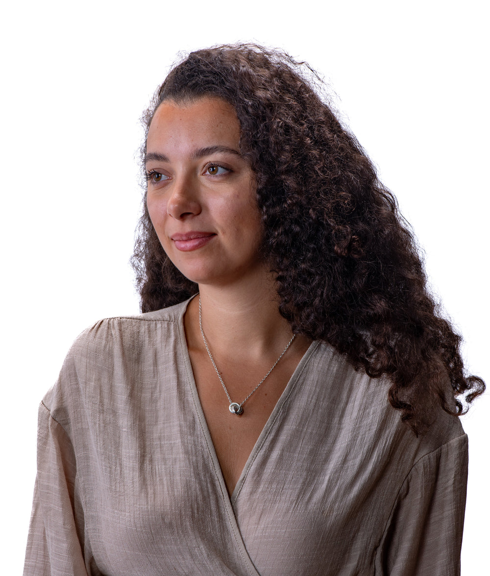 Woman with long, curly hair wearing a silver interlocking circle necklace with beige top on a white background