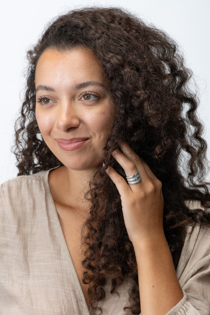Woman with curly hair wearing a small scallop silver ring touching her face against a white background