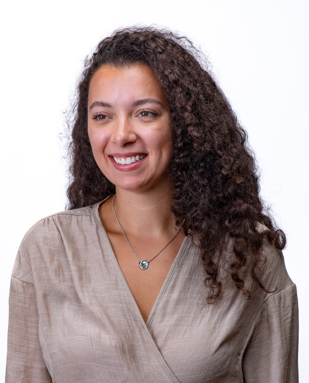 Woman with curly hair wearing a silver circle pendant with beige top on a white background